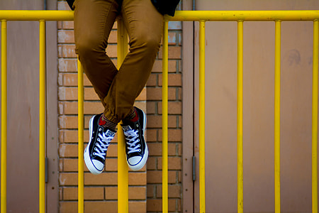 person sitting on yellow metal fence thumbnail