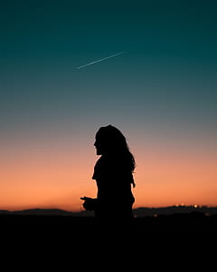 silhouette of woman with long hair against orange and green sky with meteor thumbnail