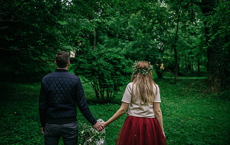 man and woman holding hands while walking on green grass field thumbnail