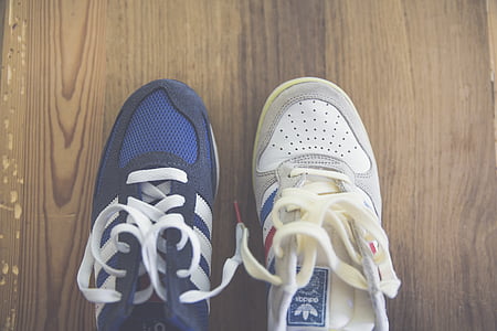 two unpaired blue and white adidas running shoes on brown wooden floor thumbnail