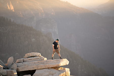 man standing on rock cliff with mountain background during daytime thumbnail