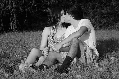 grayscale photo of couple sitting on grass while kissing thumbnail