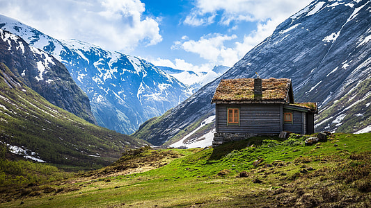 photo of brown wooden house on top of green hill near snow mountains during day time thumbnail