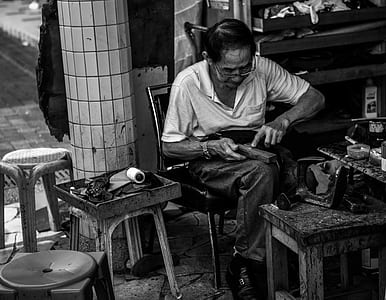 grayscale photo of man repairing shoe thumbnail