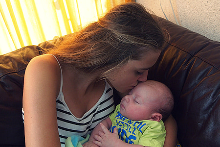 woman in white and black stripes spaghetti strap top while carrying baby kissing baby's forehead thumbnail