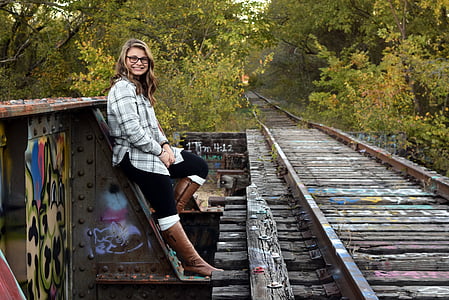woman in gray and white plaid dress shirt leaning in metal train rail road thumbnail