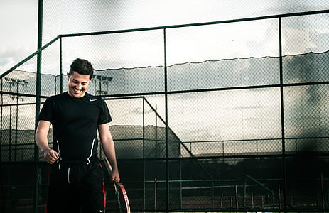 man smiling while standing and holding tennis racket thumbnail