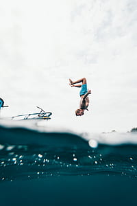 person wearing blue shorts flipping out on boat viewed half on underwater during daytime thumbnail