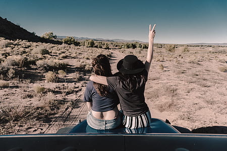 two woman sitting on vehicle hood while raising hand thumbnail