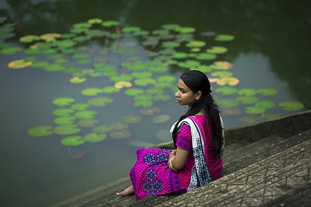 Woman in Pink Sari Dress Sitting on Stair Beside Body of Water thumbnail