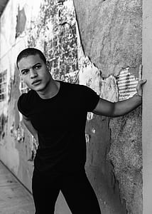 grayscale photo of man in shirt leaning on wall thumbnail