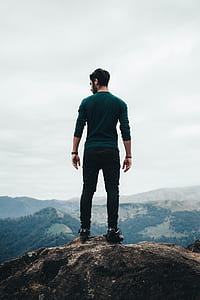 man standing on rocky mountain under white sky during daytime thumbnail