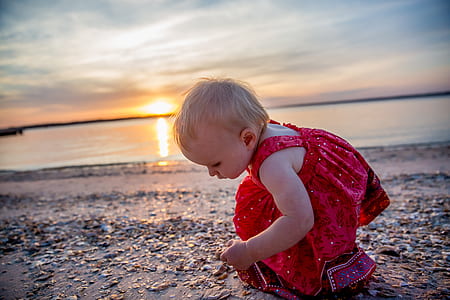 toddler wearing red dress standing on gray sand near seashore thumbnail