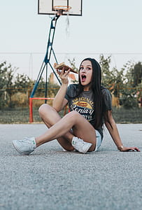 woman sitting on basketball court eating pizza thumbnail