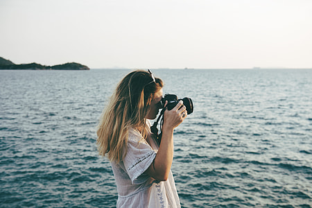 woman wearing white shirt holding camera taking photo of ocean during daytime thumbnail