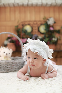baby wearing white headdress beside gray wicker basket thumbnail