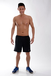 smiling man wearing black Nike shorts and blue-and-black low-top sneakers standing on white floors thumbnail