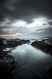 body of water with rock under cloudy sky thumbnail