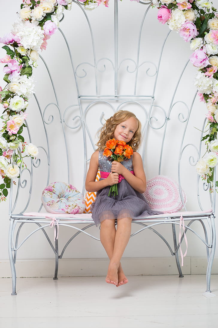 girl holding flowers wearing dress sitting on floral bench