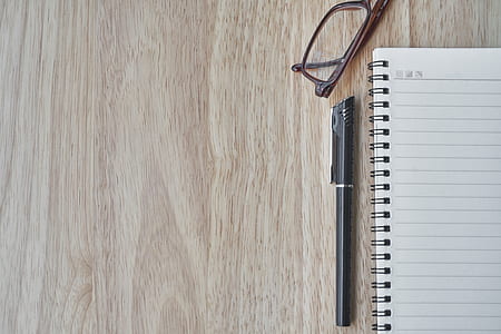 pen beside notebook and eyeglass on wooden surface thumbnail