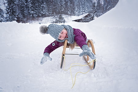 toddler girl wearing purple coat and gray hat on sled at daytime thumbnail