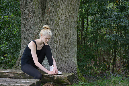 woman wearing black tank top sits on brown bench near tree during daytime thumbnail