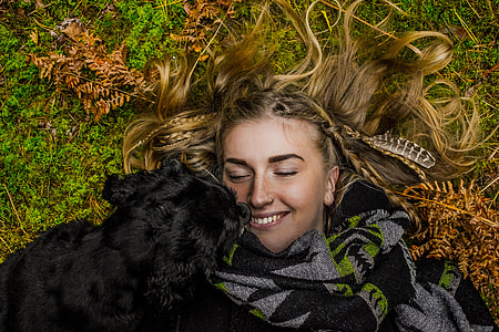 woman lies on grass field with black spaniel thumbnail