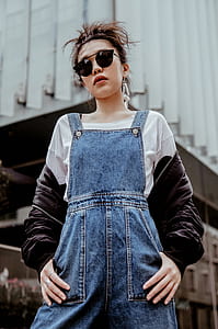 woman in blue dungarees standing near building thumbnail