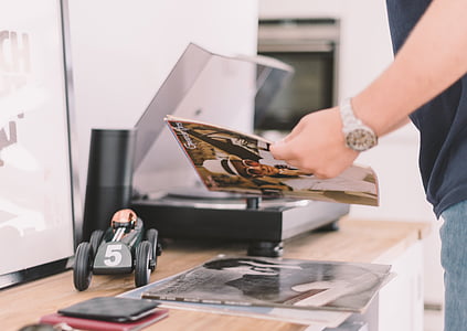 person standing near brown table holding magazine thumbnail