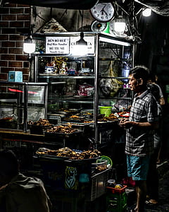 man standing beside food cart during nighttime thumbnail