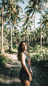 woman standing on brown soil surround by coconut trees during daytime thumbnail