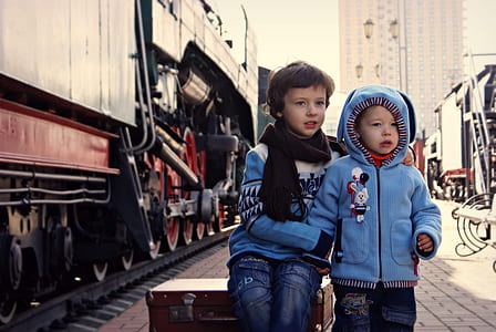 two toddler's sitting on luggage near train during day thumbnail