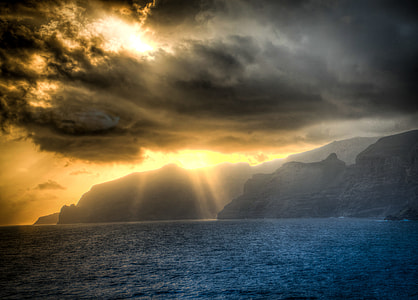 landscape photography of golden hour on sea near hills under nimbus clouds thumbnail