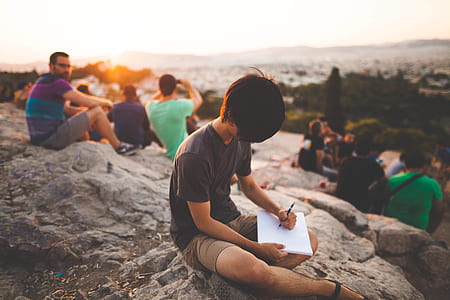 group of people sitting down on rock near body of water thumbnail