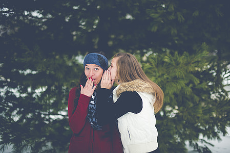 woman whispering to other woman near tree thumbnail
