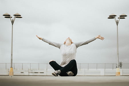 woman wearing gray cable-knit sweater, distressed blue denim jeans, and pair of sneakers sitting on concrete open field during daytime thumbnail