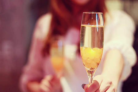selective focus photo of woman holding flute glass with brown liquid substance thumbnail