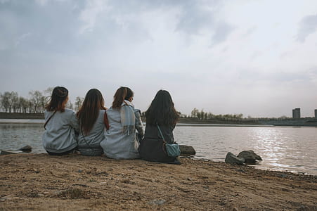 four women sitting on brown sands near body of water thumbnail