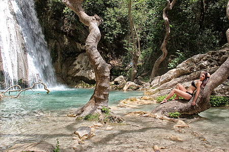 woman wearing black bikini lying on brown tree trunk beside waterfalls during daytime thumbnail
