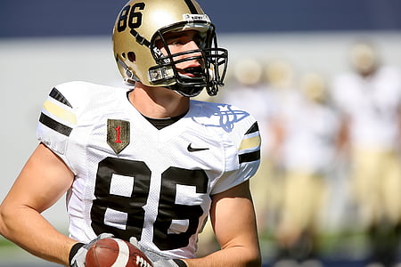 football player holding brown football during daytime thumbnail