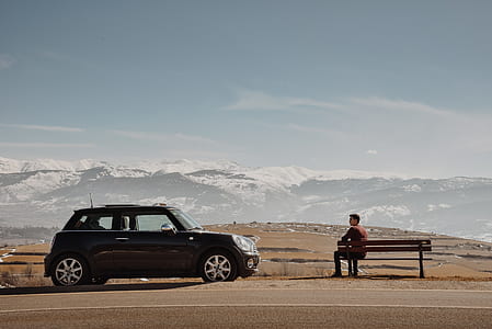 person sitting on brown bench beside black car thumbnail