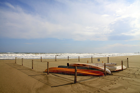 orange and white kayak inside the fence on seashore thumbnail