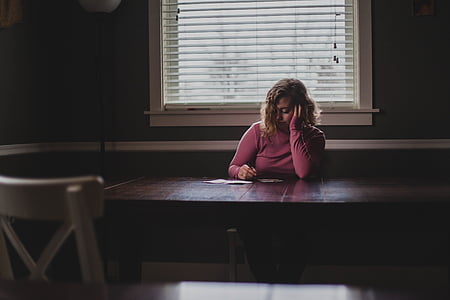 photography of woman in pink sweatshirt writing on table thumbnail