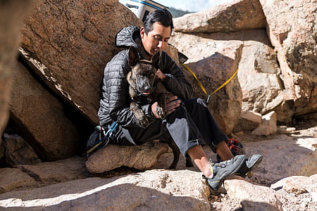 man carrying dog while sitting on stone thumbnail