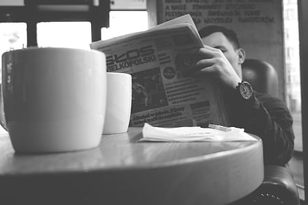 grayscale photography of man reading newspaper sitting on leather sofa thumbnail