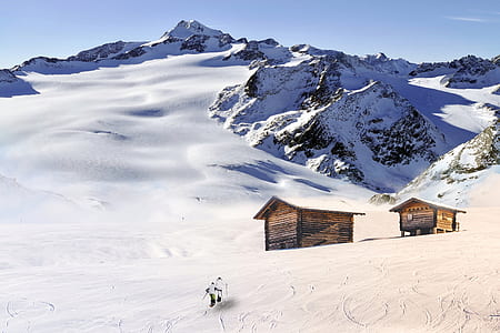 two persons walking on snow field toward house at daytime thumbnail