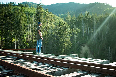 man standing on brown railroad near green leafed trees thumbnail