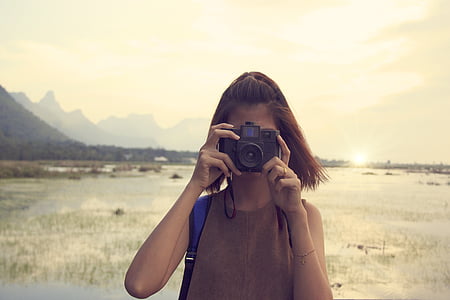 woman holding camera standing near the body of water at daytime thumbnail