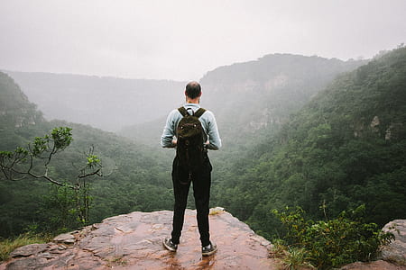man standing on top of thew mountain near trees during daytime thumbnail