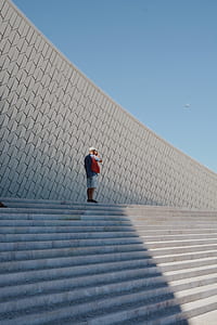 man standing alone on top of staircase holding phone on his ears with airplane flying in the sky background thumbnail